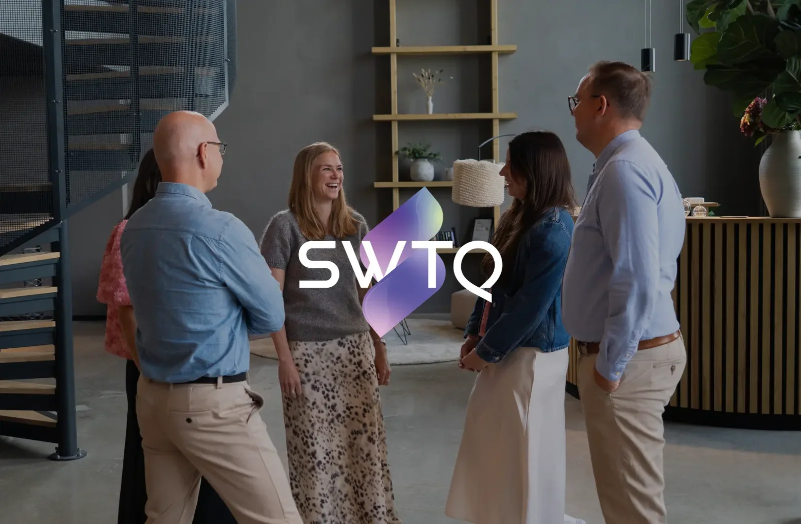 Medarbetare på SWTQ samtalar i kontorsloungen med SWTQ:s logotyp över bilden