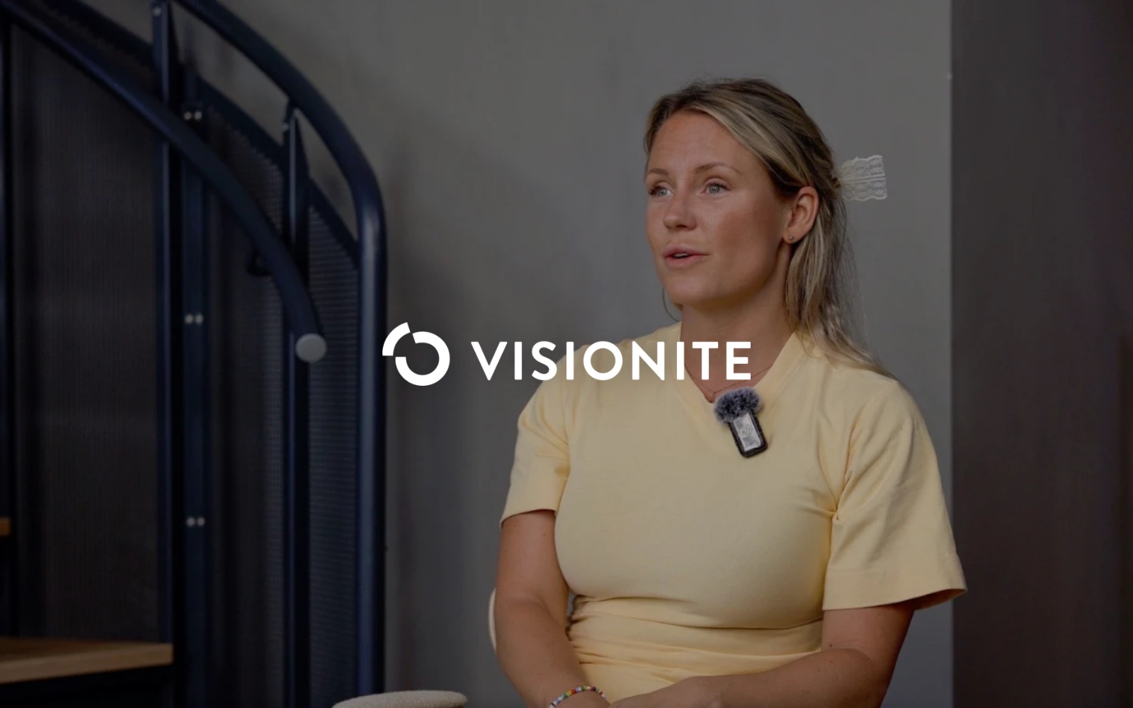 Visionites logotyp i vitt centrerad över en intervjubild med en kvinna i gul t-shirt